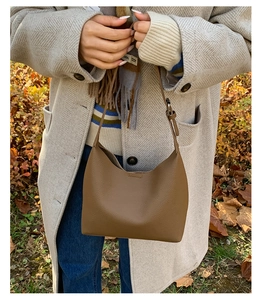 Close-up of brown pebbled leather bucket bag with adjustable strap in an outdoor setting