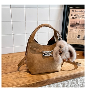 Detail of a brown lychee leather bucket bag with silver bow buckle and rabbit plush charm