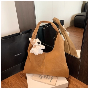 Detail of caramel suede tote bag with vertical stitching and bear charm on wooden floor