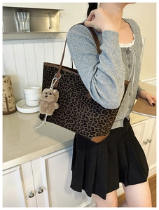 Detailed shot of leopard print tote bag featuring a plush bear charm and brown leather straps