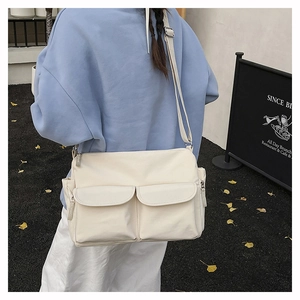Detail view of cream nylon crossbody bag with double front flap pockets and adjustable strap