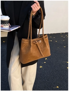 Detail of caramel brown tote bag showing matte texture and metal buckle in street setting