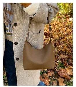 Close-up of brown textured leather bucket bag styled with a beige autumn coat