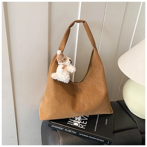Detail of tan suede hobo bag with stitching and cute plush doll pendant on a book