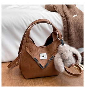 Detailed view of a brown bucket bag with silver buckle and plush rabbit keychain on wood