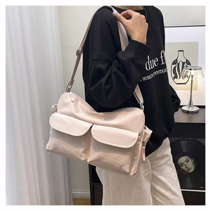 Detail of beige nylon crossbody bag with double front flap pockets on model in a modern room