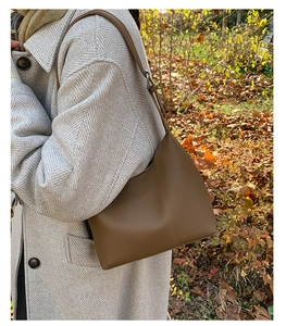 Detail of a brown leather hobo bucket bag with pebbled texture and metal buckle on strap