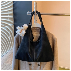 Detail of black leather tote bag with white contrast stitching and plush bear charm