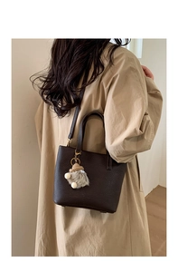 Detail of a deep brown lychee grain bucket bag with a cute plush charm on a long trench coat