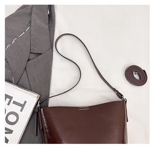Detail of the adjustable shoulder strap and smooth coffee brown leather on the bucket bag