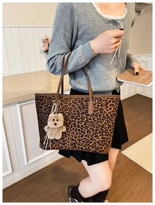 Macro detail of leopard print tote bag featuring brown leather handles and plush bear charm