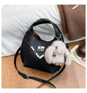 Detail of black lychee grain leather bucket bag with silver hardware and plush bunny charm