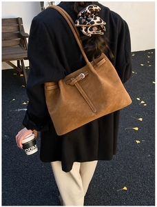 Close-up of a large brown suede tote bag featuring silver buckles in an autumn setting