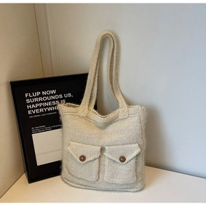 Détail du sac cabas en tricot beige avec des poches frontales et des boutons en bois marron
