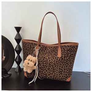 Detail view of leopard print canvas tote bag with brown leather trim and plush puppy charm