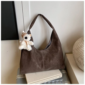 Detail of dark brown suede tote bag with contrast stitching and cute plush bear charm