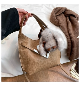 Detail of tan pebble leather bucket bag with silver metal bar and fuzzy bunny charm
