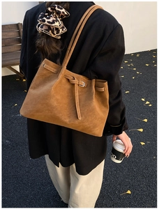 Brown matte PU tote bag with strap detail and metal buckle in an autumn outdoor setting