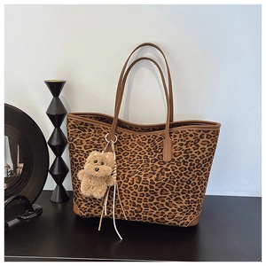 Close-up of leopard print tote bag featuring brown leather trim and plush bear charm