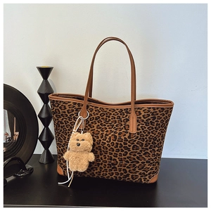 Detail of leopard print tote bag featuring brown leather straps and a plush bear charm
