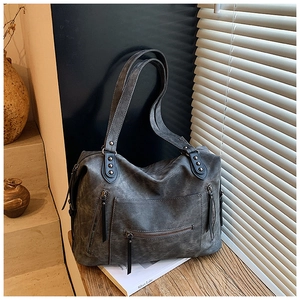 Gros plan d'un sac cabas gris vintage avec poches zippées et détails de rivets sur une table