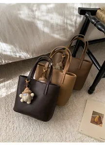 Detailed close-up of litchi grain bucket bags in three brown shades with cute plush charms