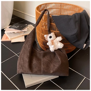 Detail of dark brown suede tote bag featuring white contrast stitching and plush bear charm