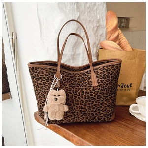 Close-up of a leopard print tote bag on a wooden table with a plush bear charm