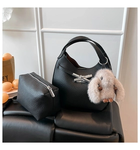 Close-up of black lychee grain leather bucket bag with silver bow and plush bunny charm