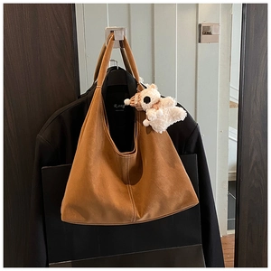 Close-up of brown suede tote bag featuring white stitching and a cute plush lamb pendant