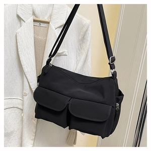 Detail view of black nylon crossbody bag with dual front flap pockets and silver hardware
