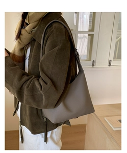 Close-up of taupe litchi grain leather bucket bag with adjustable strap on a model