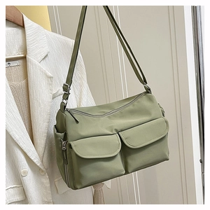 Detail of adjustable strap and front utility pockets on the green nylon crossbody bag
