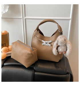 Close-up of brown pebbled leather bucket bag set with cross metal buckle and plush bunny charm