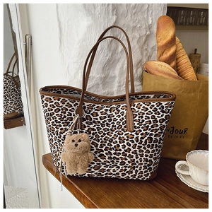 Detail of leopard print tote bag with brown leather handles and a plush bear charm