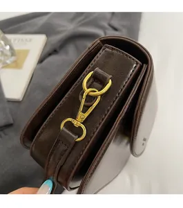 Detail of dark brown crossbody bag with glossy finish and gold metal hook hardware