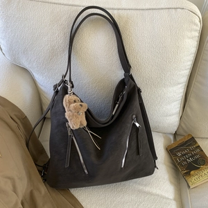 Detail of dark brown matte leather tote bag with silver zippers and plush bear charm