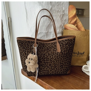 Detail of leopard print tote bag with brown leather straps and plush bear charm