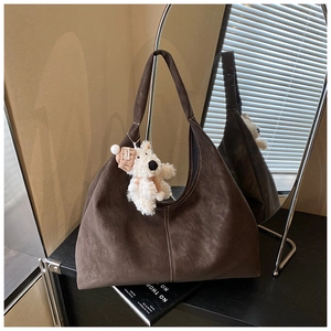 Detail view of deep brown suede hobo bag with cute white plush puppy charm and wide strap