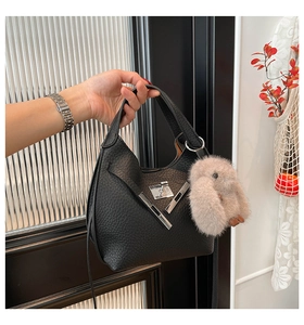 Close-up of black lychee leather bucket bag with V-shaped metal lock and plush rabbit charm