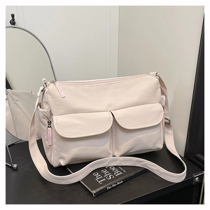 Detail view of double front pockets with zipper closure on a cream nylon crossbody bag