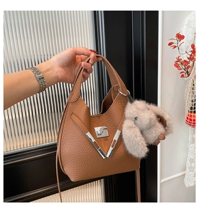 Detail of brown litchi pattern leather bucket bag with metal V-buckle and plush bunny charm