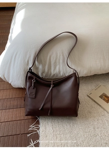 Détail d'un sac bandoulière en cuir marron foncé avec nuds décoratifs et style minimaliste