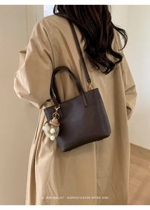 Detail of minimalist dark brown bucket bag with a straw hat charm worn over a khaki trench coat