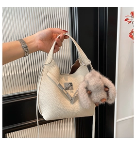 Detail of white litchi pattern leather bucket bag with silver V-buckle and plush rabbit toy