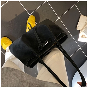 Detailed top view of a large black suede tote bag with leather buckle on a tiled floor