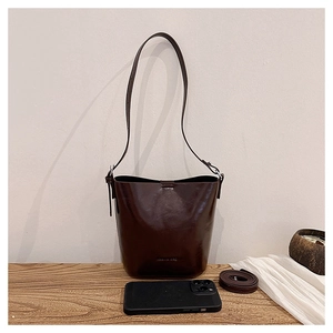 Macro shot of dark brown glossy leather bucket bag with embossed logo and adjustable strap
