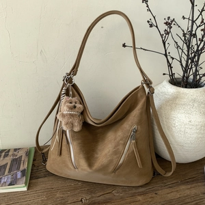 Detail of brown suede tote bag featuring parallel zippers and a cute plush bear pendant