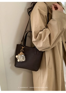 Close-up of brown pebbled leather tote bag with a cute plush doll charm and retro vibe
