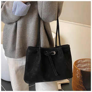 Detail view of stylish black matte leather tote bag with decorative buckle on a shoulder
